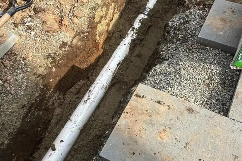 A utility line bedded in a stone trench alongside poured concrete pads on a Connecticut site.