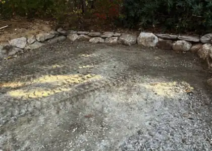 A gravel pad graded flat against a fieldstone retaining wall.
