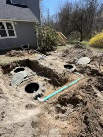 Concrete septic tanks and risers set into an open excavation beside a house.