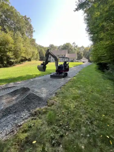 An excavator working a driveway with gravel stockpiled alongside it.