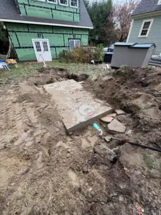 A concrete tank lid set into an open excavation beside a green house.