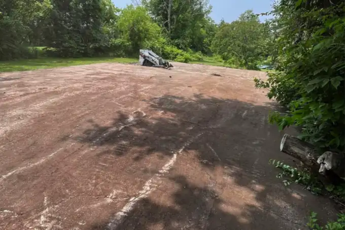 A large area stripped back to bare soil and graded flat, equipment parked at the treeline.