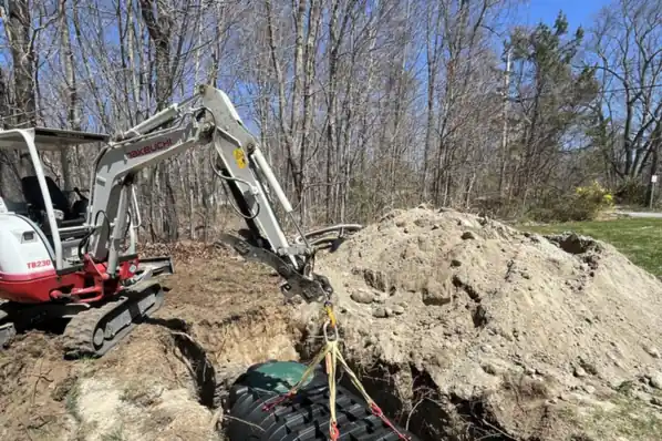 An excavator lowering a black septic tank into an open excavation on a Connecticut property.